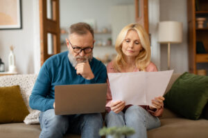 Older an and woman sitting on couch reviewing documents and looking at laptop